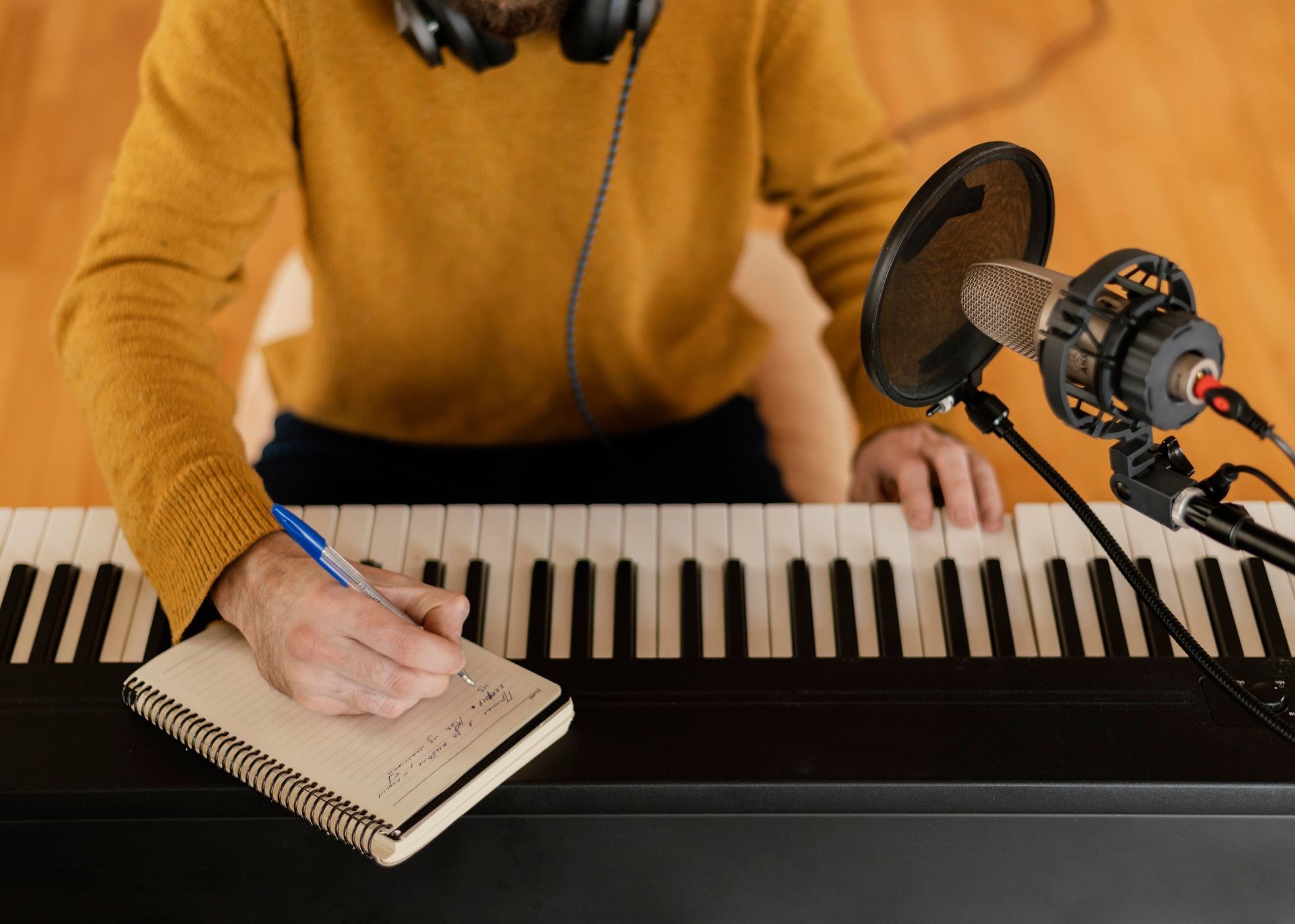 Person writing notes on a pad while playing a keyboard, with a microphone in the foreground.