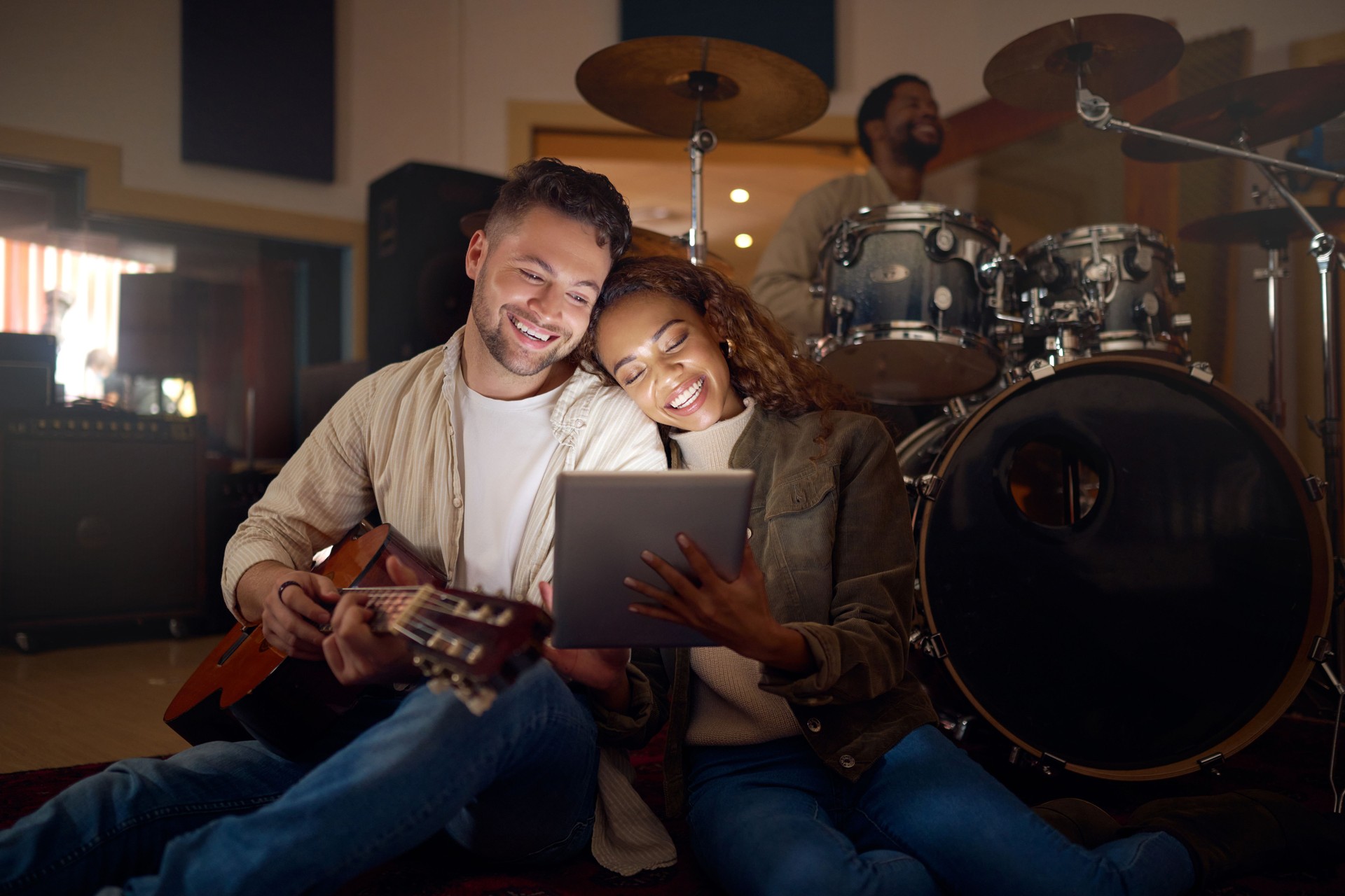 Guitar, musician couple and tablet in studio for music production or social media. Musicians, diversity love and happy man and woman with acoustic instrument and technology for web scrolling at night